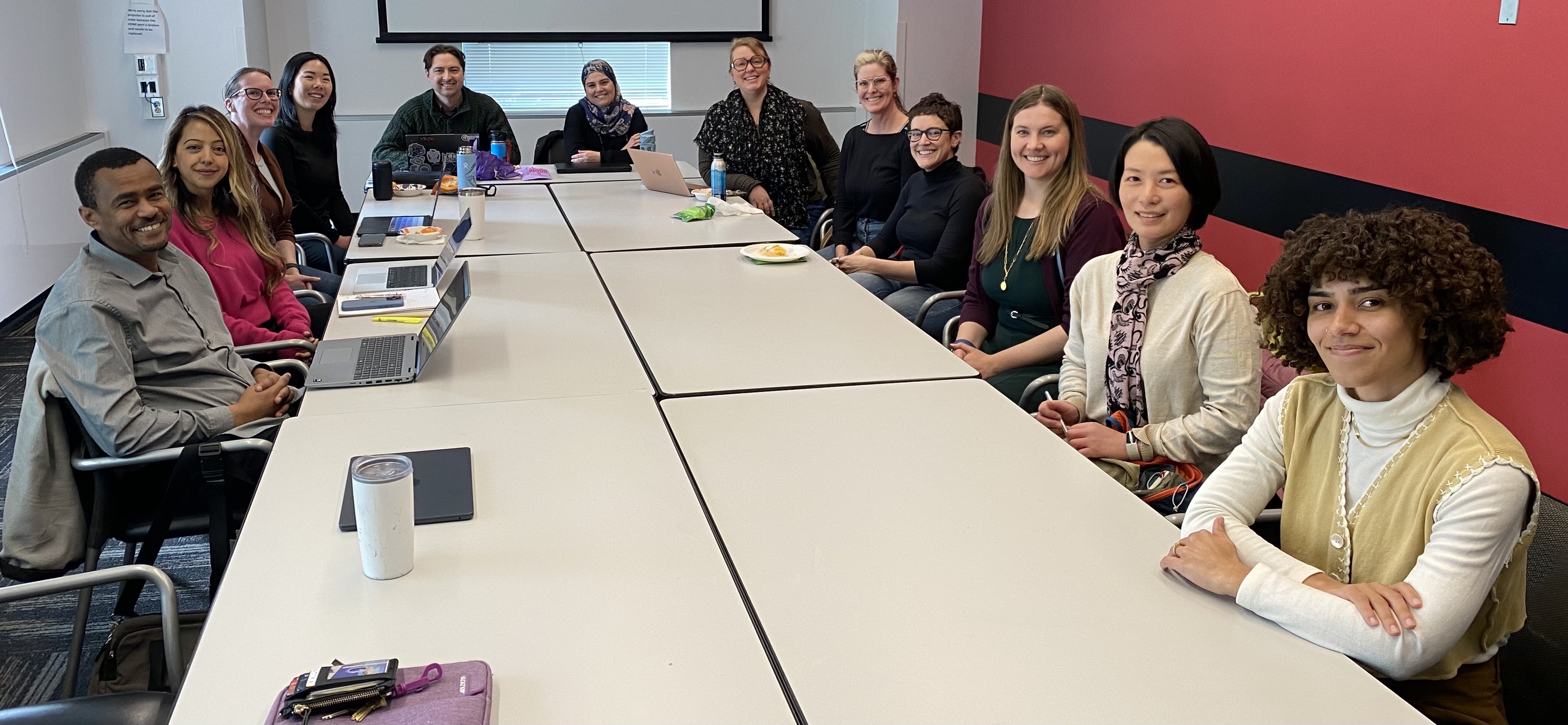 12 people sitting at a long conference table, smiling