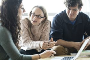 People discussing a topic while sitting in front of a shared laptop.