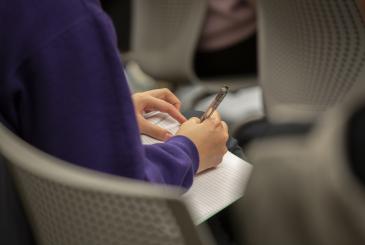 A person in a purple shirt writes in a journal.