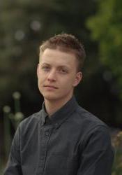 A medium length portrait of Jacob Wilson in front of greenery